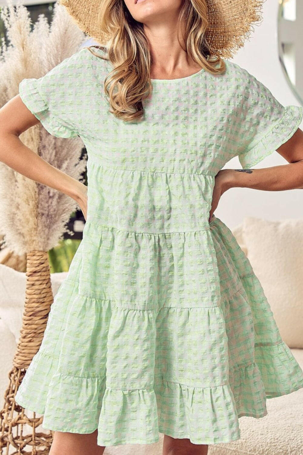 Woman wearing a light green textured short sleeve tiered mini dress with ruffle sleeves and a flowing skirt