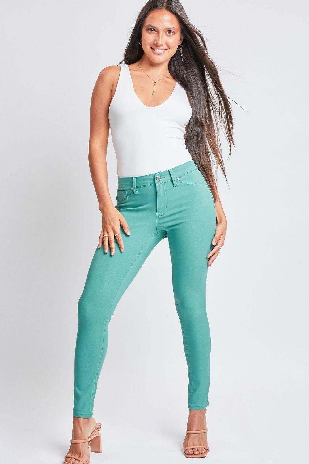 Woman wearing teal YMI Jeanswear hyperstretch mid-rise skinny pants with white sleeveless top and beige heels
