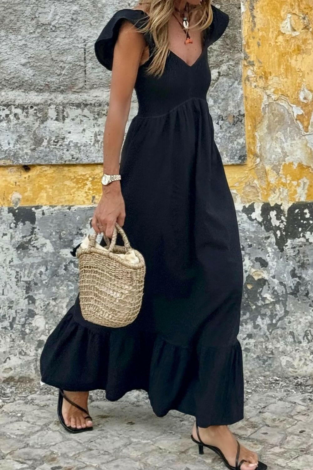 Black V Neck ruffled cap sleeve smocked maxi dress worn with straw handbag and black sandals outdoors