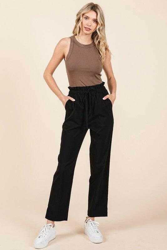 Woman wearing black Mittoshop paperbag waist tapered straight pants with brown sleeveless top and white sneakers