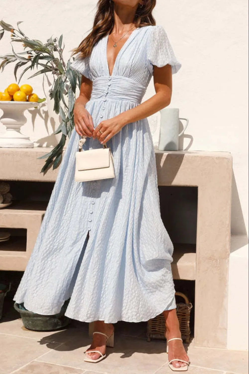 Light blue V-neck puff sleeve midi dress with smocked waist and decorative buttons, made of 100% cotton.