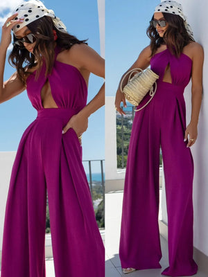 Woman wearing a purple wide leg cutout halter neck jumpsuit with crisscross and tied back details.