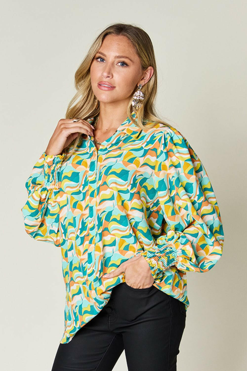 Woman wearing a colorful Double Take Full Size printed smocked long sleeve blouse with puffed sleeves and a relaxed fit.