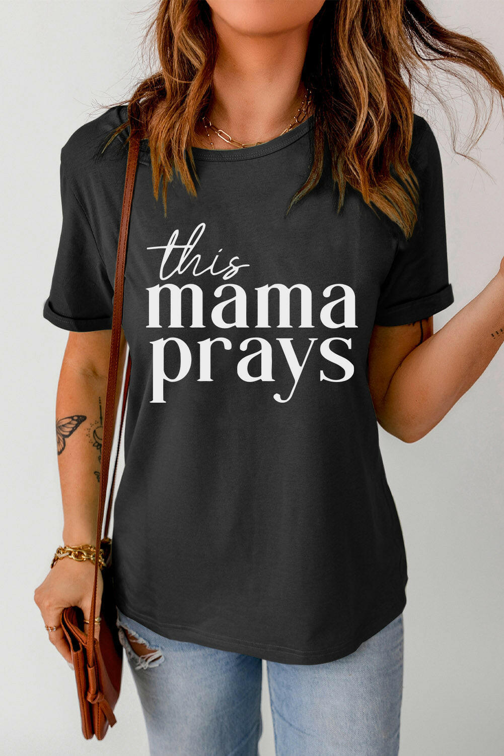 Black THIS MAMA PRAYS Graphic Tee with short sleeves and round neck worn with jeans and brown purse