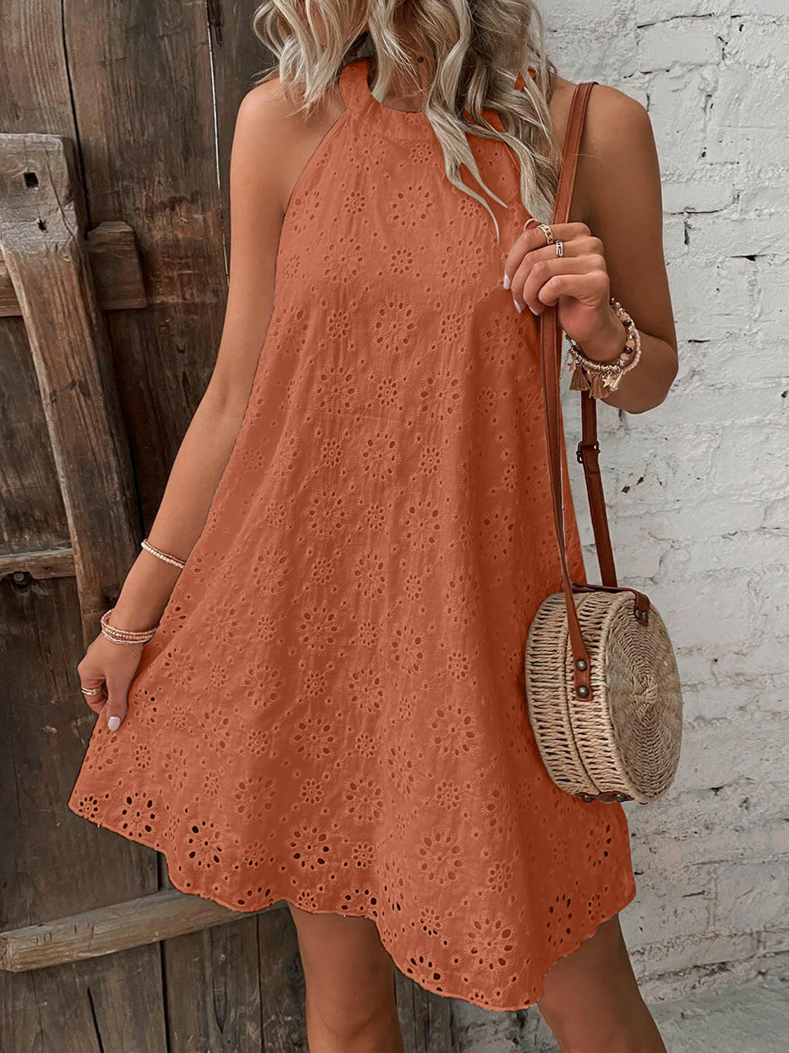 Woman wearing a rust-orange eyelet Grecian neck mini dress holding a round wicker handbag.