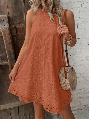 Woman wearing a rust-orange eyelet Grecian neck mini dress holding a round wicker handbag.