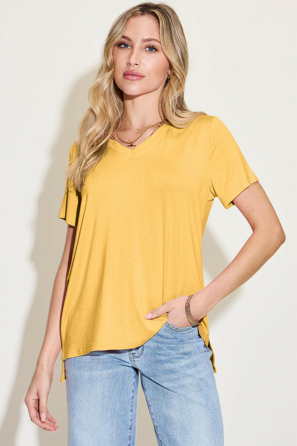 Woman wearing yellow Basic Bae Bamboo full size V-neck high-low T-shirt with short sleeves and light blue jeans